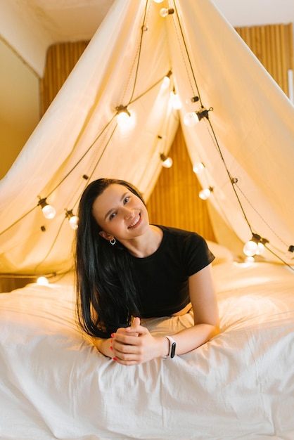 A young woman is lying in a fourposter bed with glowing light bulbs