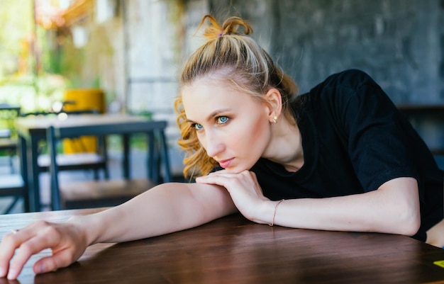 A young woman is lying on a table with a thoughtful look to the side The girl folded her hands on the table