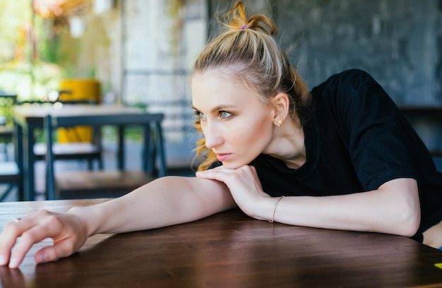 A young woman is lying on a table with a thoughtful look to the side The girl folded her hands on the table