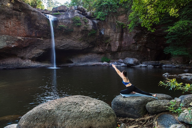 Young woman is playing yoga in front of the waterfall