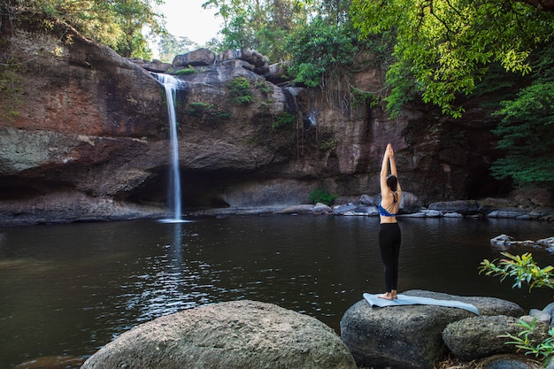 Young woman is playing yoga in front of the waterfall