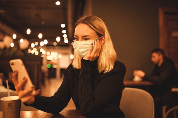 Young woman is sitting in a cafe Blond woman in mask Quarantine time