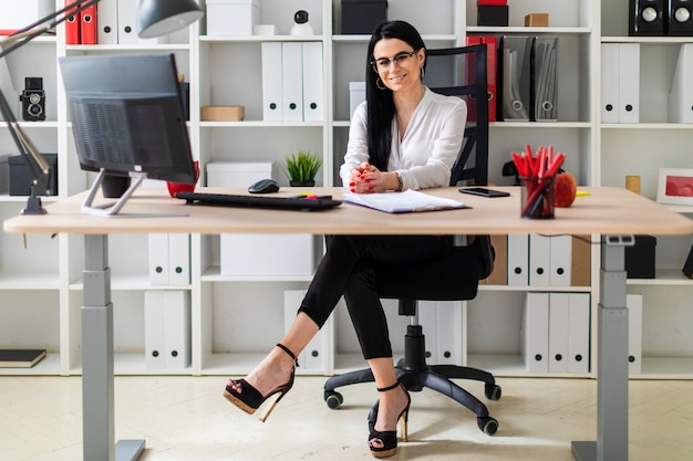 A young woman is sitting at the computer desk. Next to the woman lie documents and a marker.