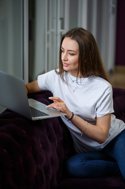 A young woman is sitting on the couch and working on a laptop remotely from work