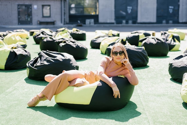 A young woman is sitting on an easy chair outdoors and enjoying a sunny day A beautiful contented girl in sunglasses