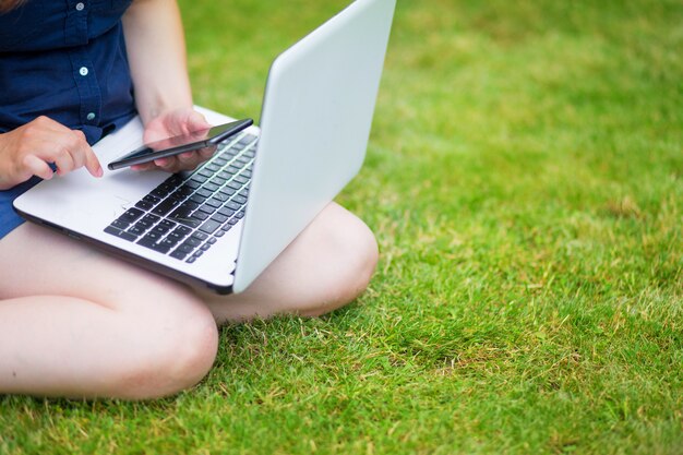 a young woman is sitting in a meadow with a laptop and talking on an online conference at work