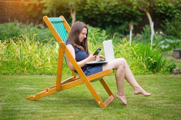 a young woman is sitting in a meadow with a laptop and talking on an online conference at work