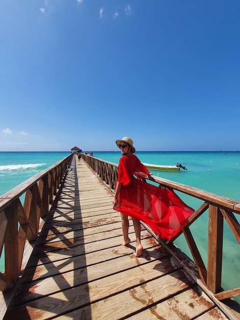 A young woman is standing by the pier in a hat