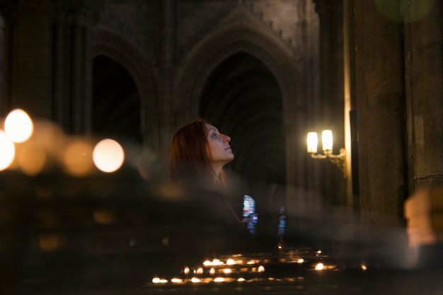 A young woman is standing in a Catholic church. Nearby are burning candles. Blurred