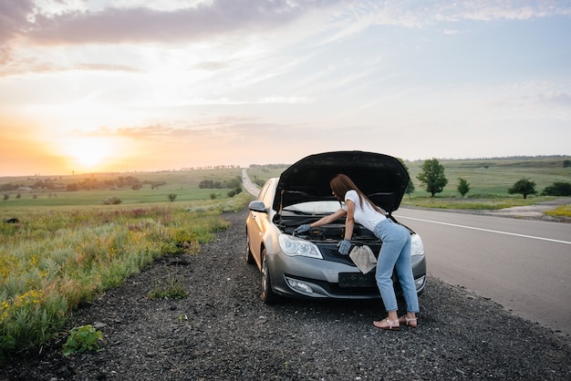 A young woman is standing near a broken-down car.

