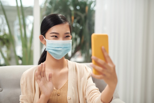 Young woman is talking by videocall in mask. Working from home, talking with friends, taking selfie in mask