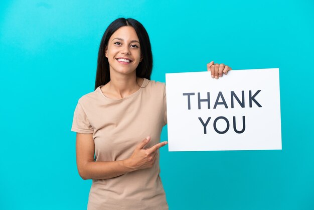 Young woman over isolated background holding a placard with text THANK YOU and  pointing it