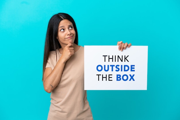 Young woman over isolated background holding a placard with text Think Outside The Box and thinking