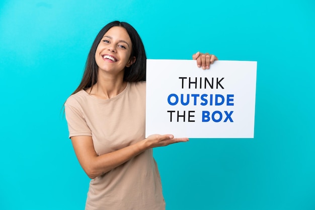 Young woman over isolated background holding a placard with text Think Outside The Box with happy expression