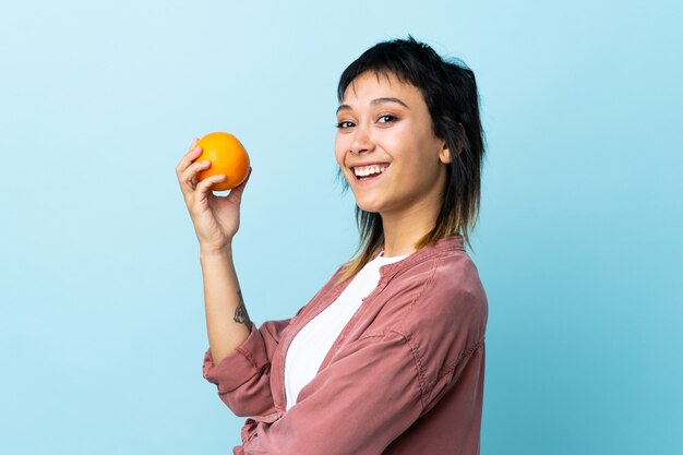 Young woman over isolated blue holding an orange