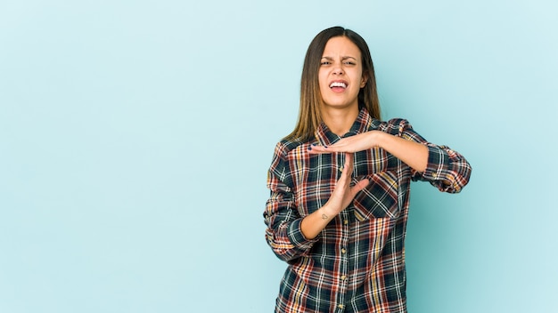 Young woman isolated on blue showing a timeout gesture.