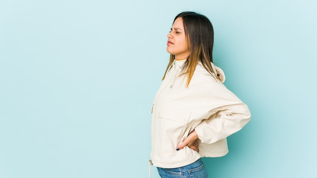 Young woman isolated on blue space suffering a back pain.