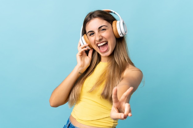 Young woman over isolated blue wall listening music and singing