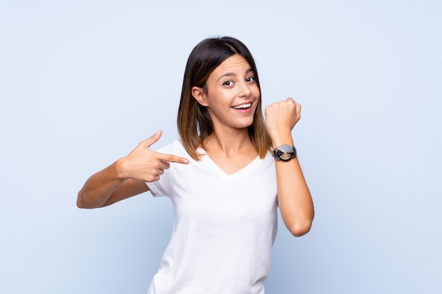 Young woman over isolated blue wall showing the hand watch