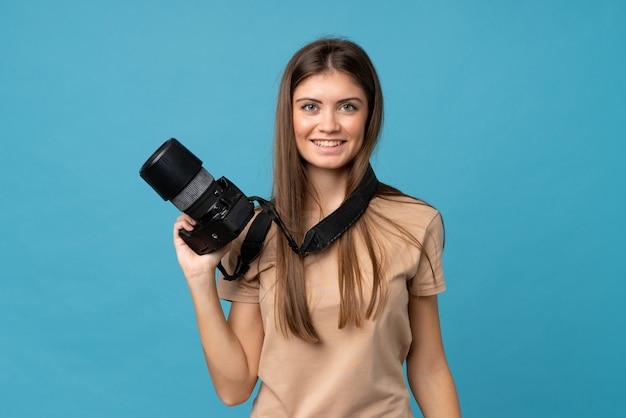 Young woman over isolated blue wall with a professional camera