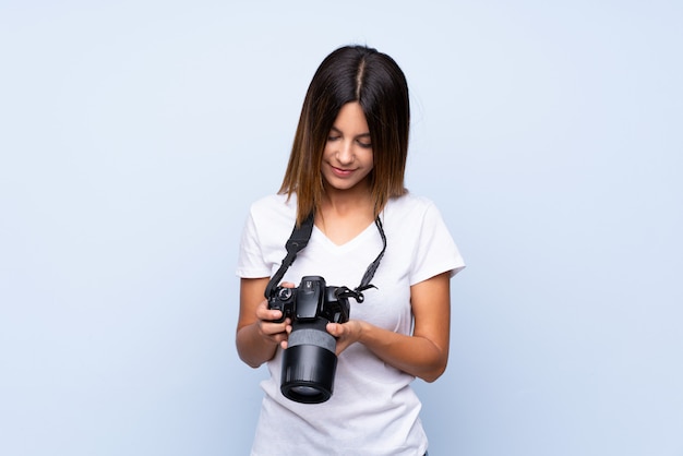 Young woman over isolated blue wall with a professional camera