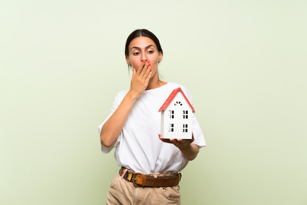 Young woman over isolated green wall holding a little house