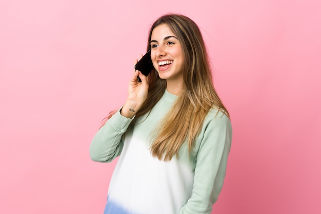 Young woman on isolated pink keeping a conversation with the mobile phone