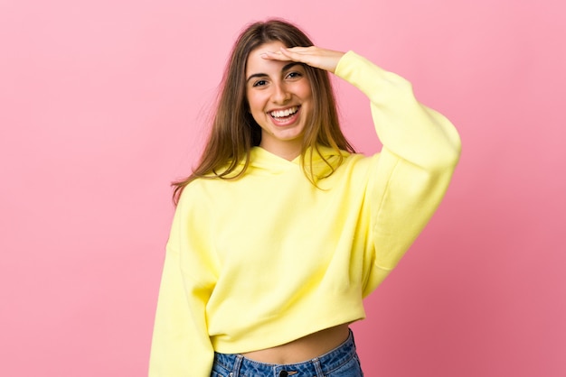 Young woman on isolated pink saluting with hand with happy expression