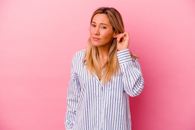 Young woman isolated on pink wall covering ears with fingers, stressed and desperate by a loudly ambient