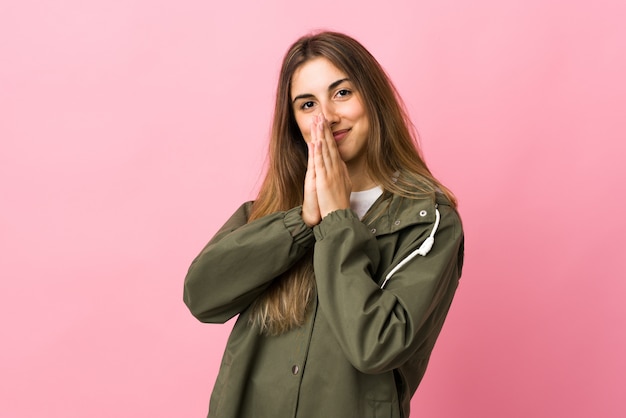 Young woman over isolated pink wall keeps palm together. Person asks for something