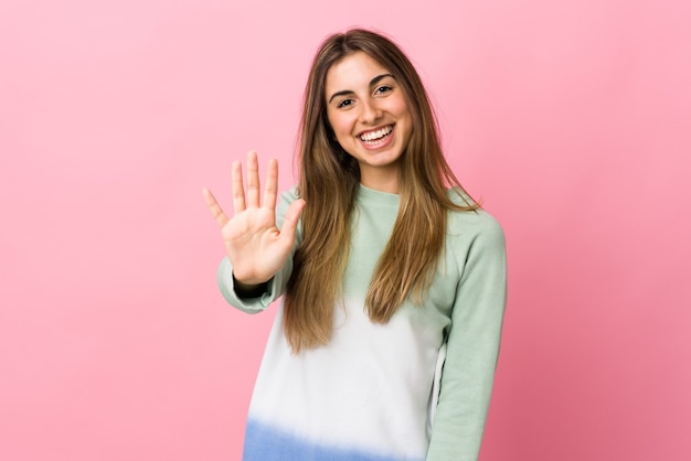 Young woman over isolated pink wall saluting with hand with happy expression