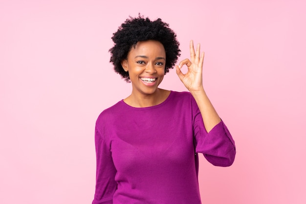 Young woman over isolated pink wall surprised and showing ok sign