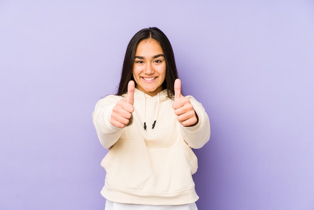 Young woman isolated on a purple background with thumbs ups, cheers about something, support and respect concept.