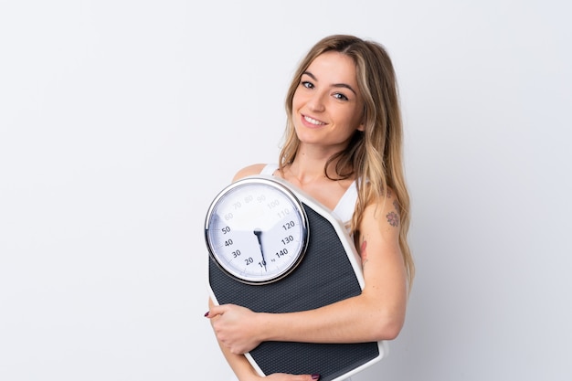 Young woman over isolated white wall with weighing machine