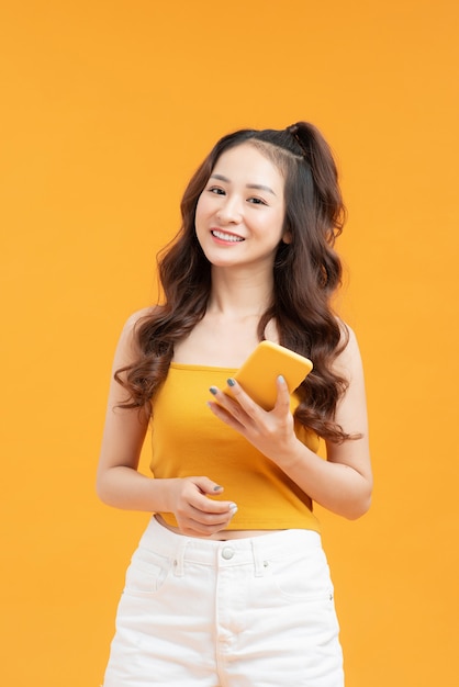 Young woman over isolated yellow background sending a message with the mobile