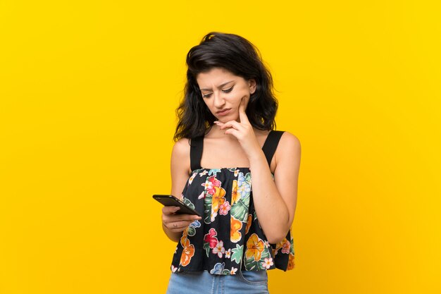 Young woman isolated on yellow  using mobile phone