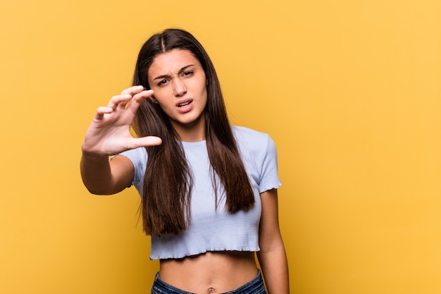 Young woman isolated on yellow wall showing claws imitating a cat, aggressive gesture.