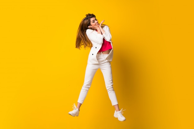 Young woman jumping over isolated yellow wall