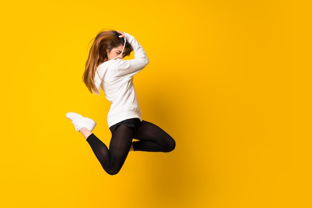 Young woman jumping over isolated yellow wall