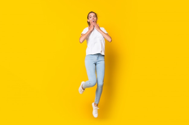 Young woman jumping over isolated yellow wall