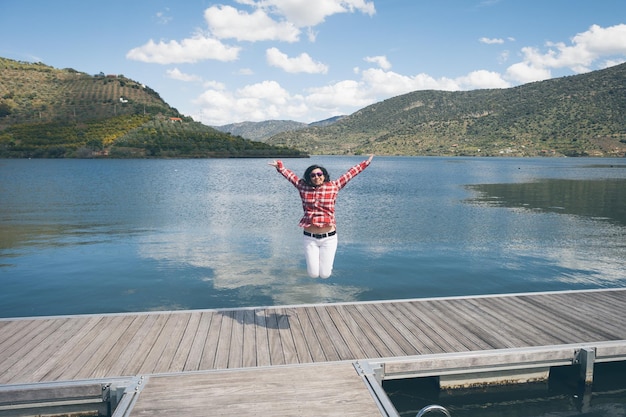 Photo young woman jumping on pier over lake against sky