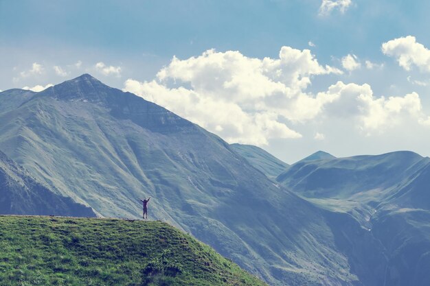 Young woman jumping with hands up against the sky and mountain xA