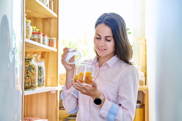 Young woman in kitchen with containers jars of food with dried apricots