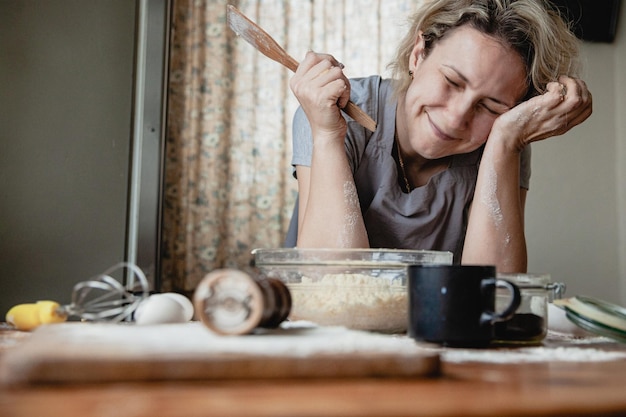 A young woman in the kitchen with a spatula in her hands in front of a bowl is upset that she does not know how to cook