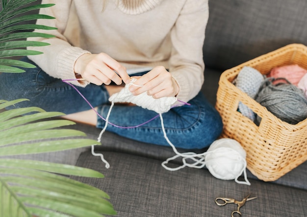 Young woman knitting warm scarf indoors