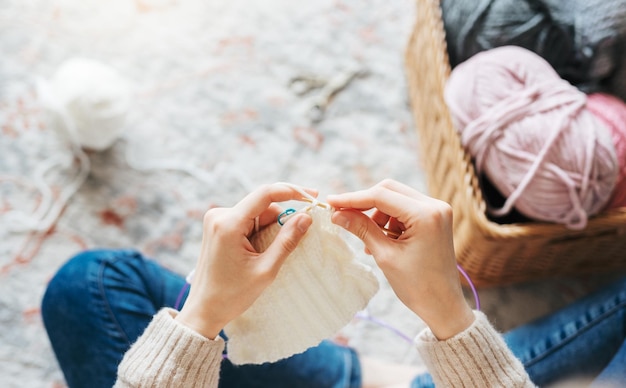 Young woman knitting warm scarf indoors