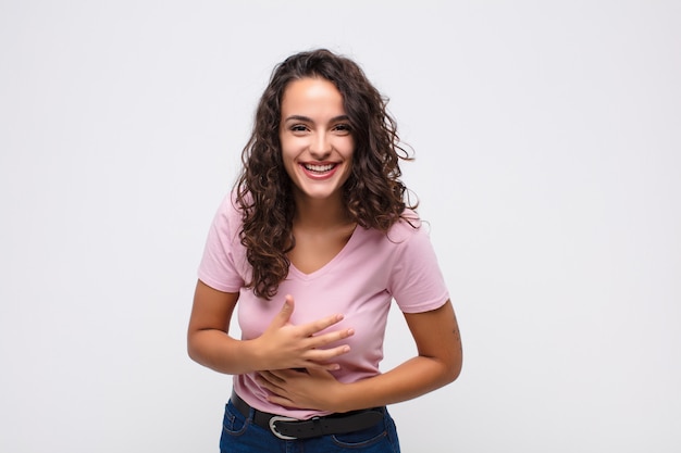 Young woman laughing out loud at some hilarious joke, feeling happy and cheerful, having fun on white wall