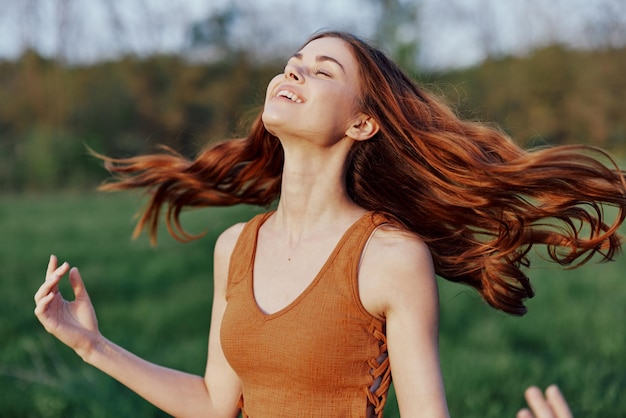 A young woman laughing and smiling merrily in nature in the park with the sunset lighting illuminating her long red hair