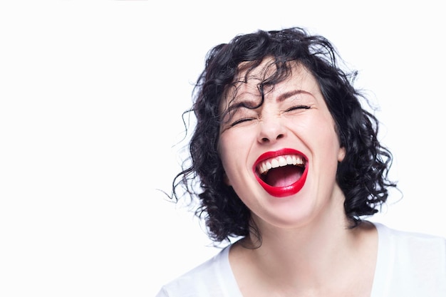 A young woman laughs contagiously with her mouth open and her eyes closed Beautiful curly brunette in a white tank top Joy and positivity White background Closeup