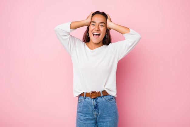 Young woman laughs joyfully keeping hands on head